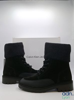 Les bottes sont noires et ornées de fourrure sur un fond blanc.