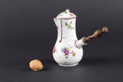 un petit vase blanc avec des fleurs et une noix posée à côté