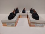 Trois paires de chaussures noires sont exposées dans une vitrine.