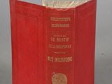 an old red book sitting on top of a table next to a gray wall