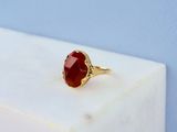 une bague en or sertie d'une pierre rouge, posée sur un bloc de marbre blanc