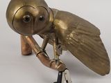 brass figurine of a bird holding a key on a white surface
