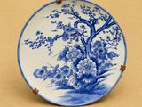 une assiette bleue et blanche décorée d'un arbre et de fleurs
