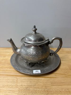 an antique silver teapot and saucer on a wooden table