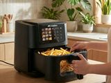 une femme en train de mettre des frites dans une friteuse à air chaud posée sur un plan de travail de cuisine