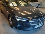 Une voiture noire est garée dans un garage, avec d'autres voitures en arrière-plan.
