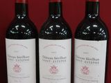 trois bouteilles de vin rouge sont alignées sur une surface rouge