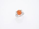 une bague sertie d'une pierre orange et de diamants, sur fond blanc