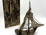 une maquette ancienne en laiton représentant un voilier, avec un livre en arrière-plan