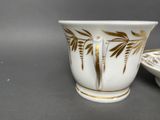 a white cup with a gold leaf design on it