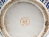 someone is holding a blue and white vase with a brown handle
