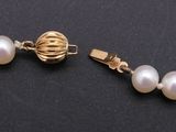 a close up of a white pearl necklace with a gold clasp