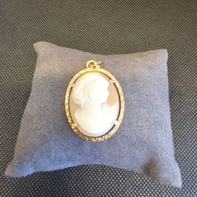 une photo d'une broche-camaïeu dorée et blanche posée sur un coussin