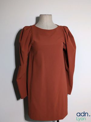 une robe orange posée sur un mannequin, devant un mur blanc