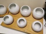 six white vases sitting on a wooden tray on a table