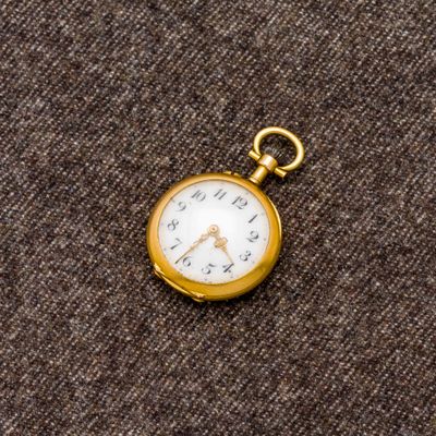 une petite montre de poche en or posée sur un tissu marron