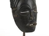 une image représentant un masque noir posé sur un socle en bois, sur fond blanc