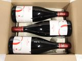 three bottles of red wine in a cardboard box on a table