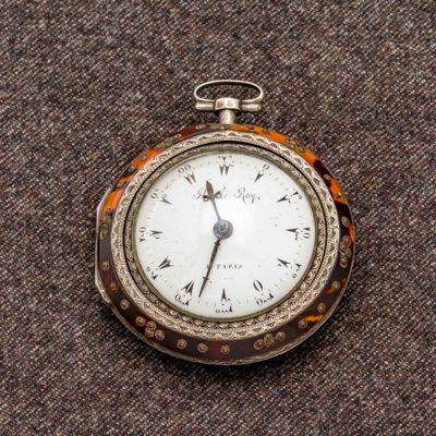 une montre de poche en argent posée sur une surface marron