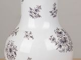 a white vase with black flowers on it sitting on a table