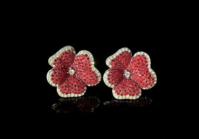 une paire de boucles d'oreilles en forme de fleurs, composées de diamants rouges et blancs, posées sur un fond noir