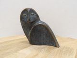 sculpture représentant un hibou posée sur une table en bois, avec un mur blanc en arrière-plan