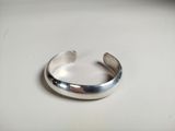 a close up of a silver cuff bracelet on a white surface