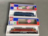 trois trains miniatures encore dans leur emballage sont posés dans une boîte sur une table