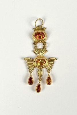 a close up of a gold pendant with a red stone on it