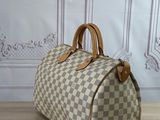 louis vuitton damier speedy bag on a wooden floor in front of a wall