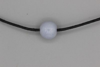 une photo d'un collier composé d'une perle blanche montée sur un cordon noir