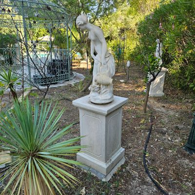 une statue représentant un homme debout sur un socle dans un jardin