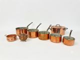 a group of copper pots and pans sitting on a white surface