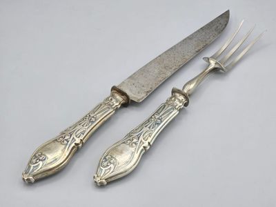 une paire de couteaux plaqués argent et un couteau posés sur une surface blanche