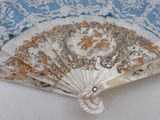a white and gold fan on a blue and white table cloth