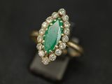 une bague sertie d'une émeraude et de diamants, exposée sur un fond noir