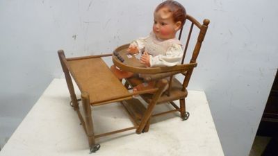 une poupée assise dans une chaise haute sur laquelle est posé un plateau