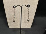 pair of silver earrings on a stand with a black background