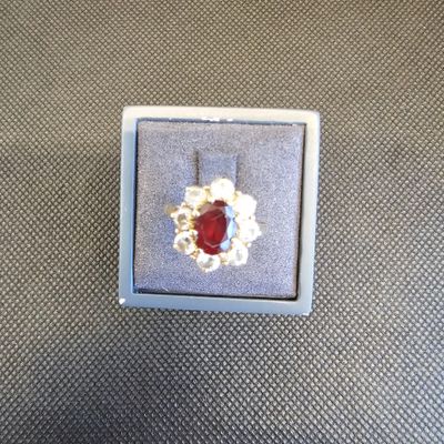 bague en argent avec une pierre rouge entourée de perles, posée sur une table