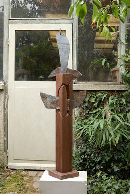 une sculpture représentant un oiseau, posée sur un socle devant un bâtiment