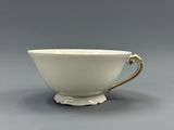 a close up of a white cup with gold handles on a gray surface