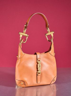 tan leather purse with gold hardware on a shiny surface