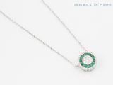 a close up of a diamond and emerald necklace on a white surface