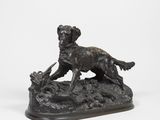 statue en bronze représentant un chien assis sur un rocher, tenant un oiseau dans la gueule