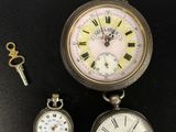 deux montres de poche anciennes et une clé posées sur une surface noire