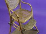 wooden chair with wicker seat and foot rest against a purple background