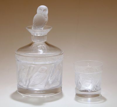 un bocal en verre orné d'un oiseau, à côté d'un verre