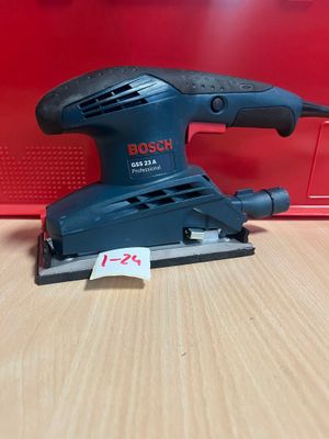 une ponceuse orbitale Bosch posée sur une table, à côté d'une boîte rouge
