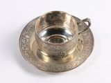 silver cup and saucer on a white surface with a white background