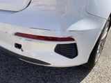 the rear end of a white car with a dented bumper